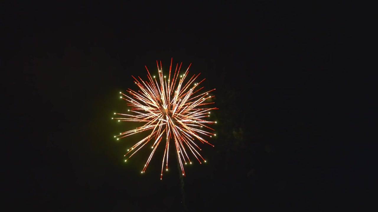 Fuochi d'artificio luminosi esplodono in diverse forme e colori su un cielo scuro. L'evento si svolge in una città di notte. Le persone si riuniscono per guardare e festeggiare insieme.