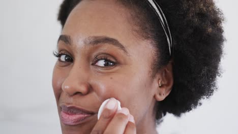 Primer-Plano-De-Una-Feliz-Mujer-Afroamericana-Limpiando-La-Cara-Con-Algodón-En-El-Baño,-Cámara-Lenta