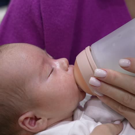 loving mother holding a baby in her arms and feeding it from the bottle. newborn child being fed from a bottle with pacifier. close up