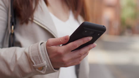 close up shot of woman outdoors on city street holding mobile phone looking at messages social media or news 2