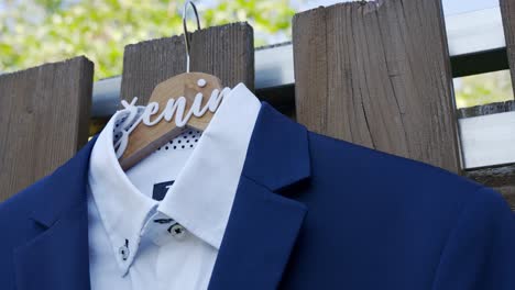 a blue suit jacket on a hanger marked with "groom" is hung on a wooden fence outdoors