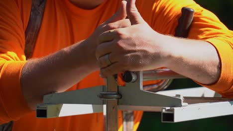 Un-Leñador-Con-Camisa-Naranja-Y-Anillo-De-Bodas-Ajusta-Su-Plataforma-De-Fresado-Con-Motosierra-Estilo-Alaska