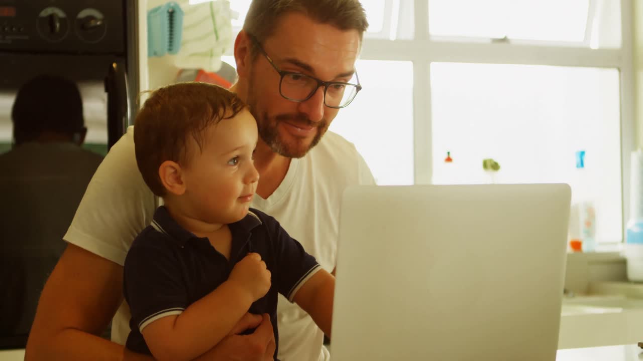 padre e hijo usando computadora portátil en la cocina 4k