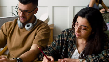 Nahaufnahme-Eines-Studenten-Mit-Kopfhörern,-Der-Mit-Einer-Kumpelin-Am-Tisch-Spricht-Und-über-Ein-Projekt-Mit-Laptop-1-Diskutiert