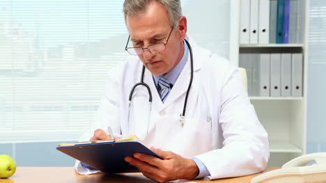 doctor writing on clipboard at his desk