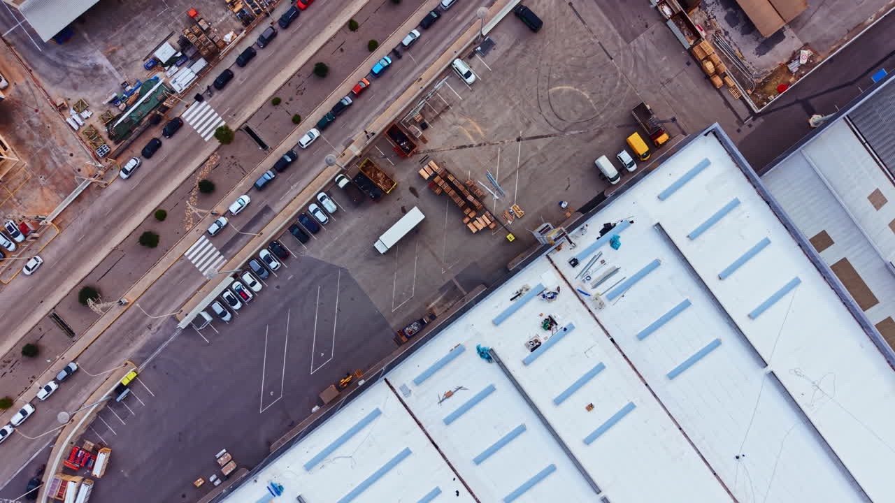 Werknemers repareren overdag het dak van een groot commercieel gebouw, terwijl voertuigen in de buurt geparkeerd staan en machines in gebruik zijn op een bouwplaats.