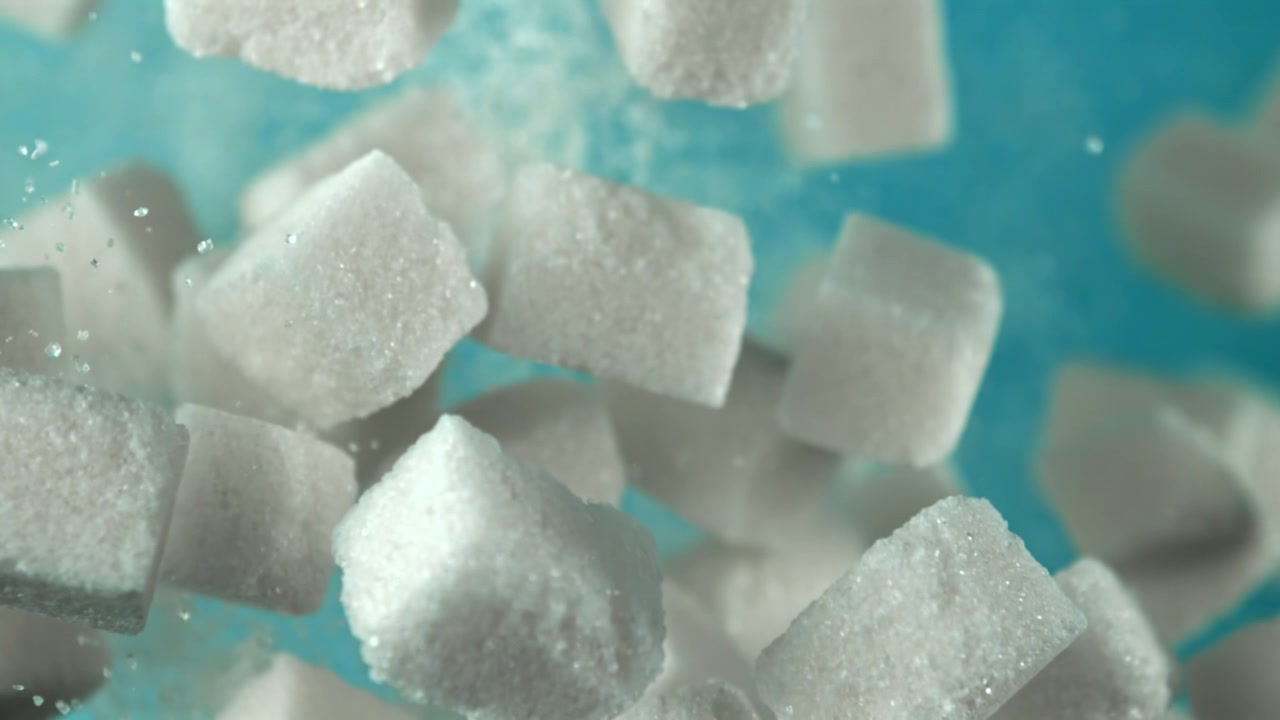 Terrones de azúcar blancos cayendo a cámara lenta sobre fondo azul
