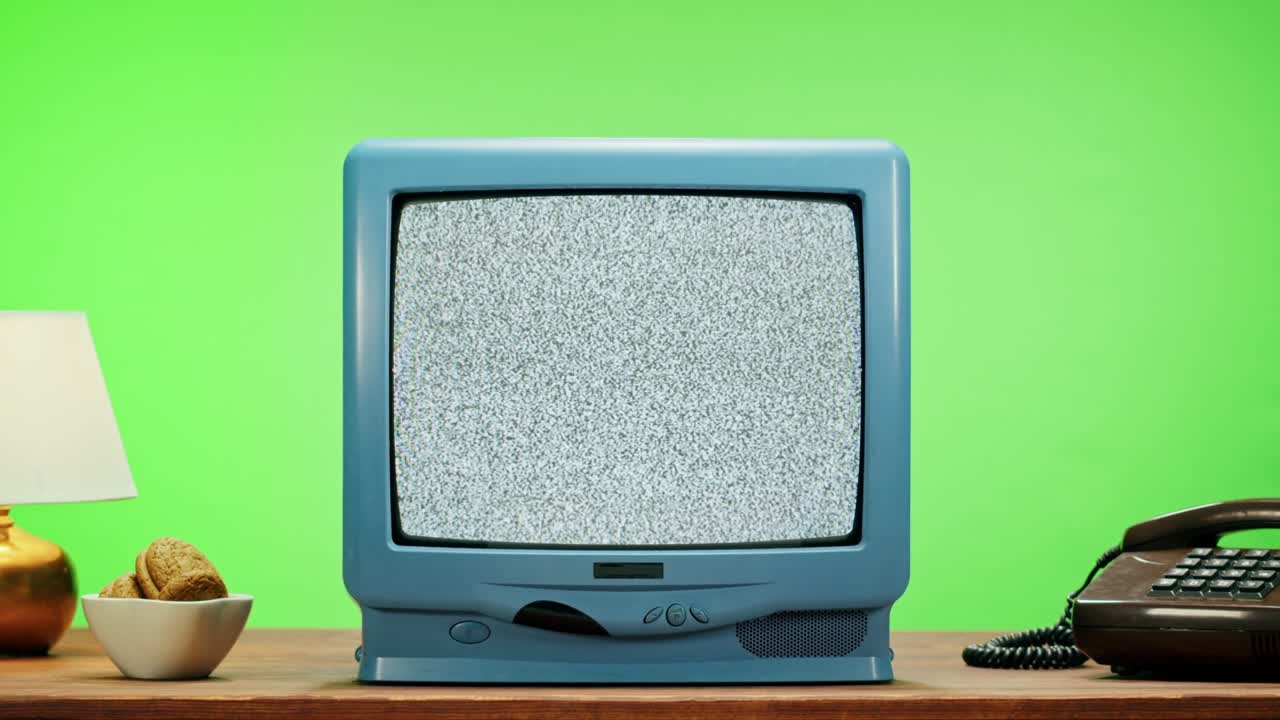 Old television with grey screen on chroma green background. Close-up of vintage tv on table with retro phone, nostalgia