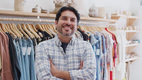 retrato del propietario masculino de una tienda de moda de pie frente a la ropa en los rieles