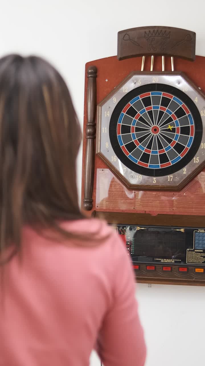 Woman throwing dart arrows at target of dartboard at home