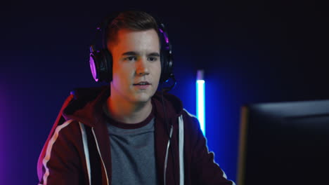 Close-Up-View-Of-Young-Man-With-Headphones-And-Playing-A-Game-On-The-Computer-And-Celebrating-A-Victory-In-A-Room-With-Colorful-Neon-Lamps-On-The-Wall