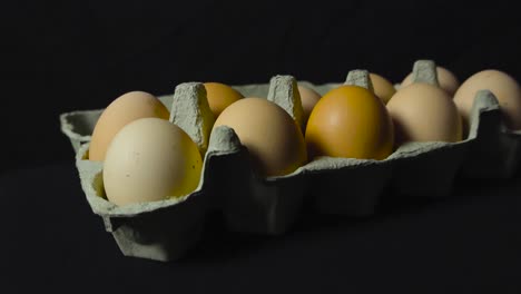 close up o close-up de huevos amarillos, marrones y blancos en una caja de cartón que se coloca sobre un fondo oscuro en una pantalla bajo luces de estudio que hacen sombras. cámara girando alrededor de ellos