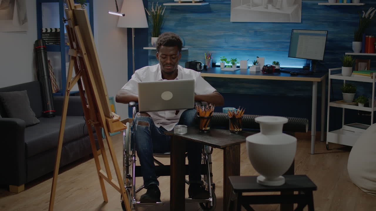 Black person in wheelchair using laptop computer for art