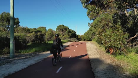 Mujer-Ciclista-Con-Casco-Montando-Su-Bicicleta-En-Una-Línea-De-Bicicletas-En-Un-Parque-En-Australia-Occidental-Después-De-Salir-Del-Trabajo-En-Un-Soleado-Día-De-Otoño---Perth,-WA