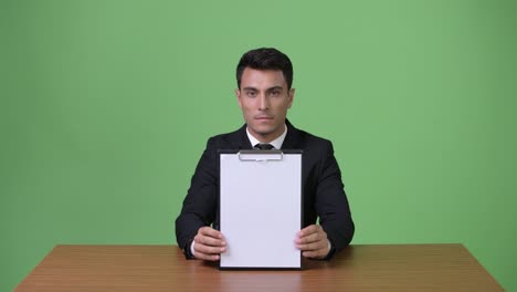 young handsome hispanic businessman against green background
