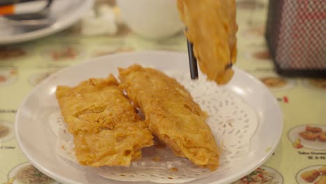 palillos para comer recogiendo el rollo de primavera de la piel de tofu frito del plato, primer plano