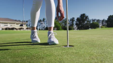 Caucasian-female-golf-player-reaching-for-a-ball-standing-on-golf-field