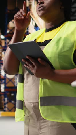 vertical video african american female staff in hi vis vest counts packages on industrial racks