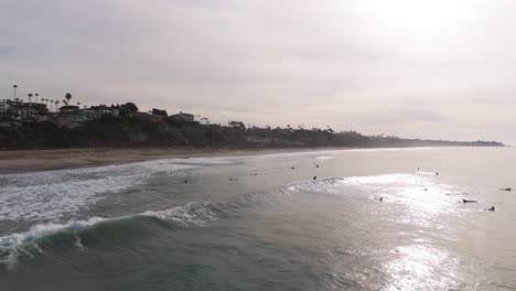 Vista-Aérea-Matutina-De-Surfistas-De-California-Montando-Olas-En-La-Ciudad-Costera-De-OC