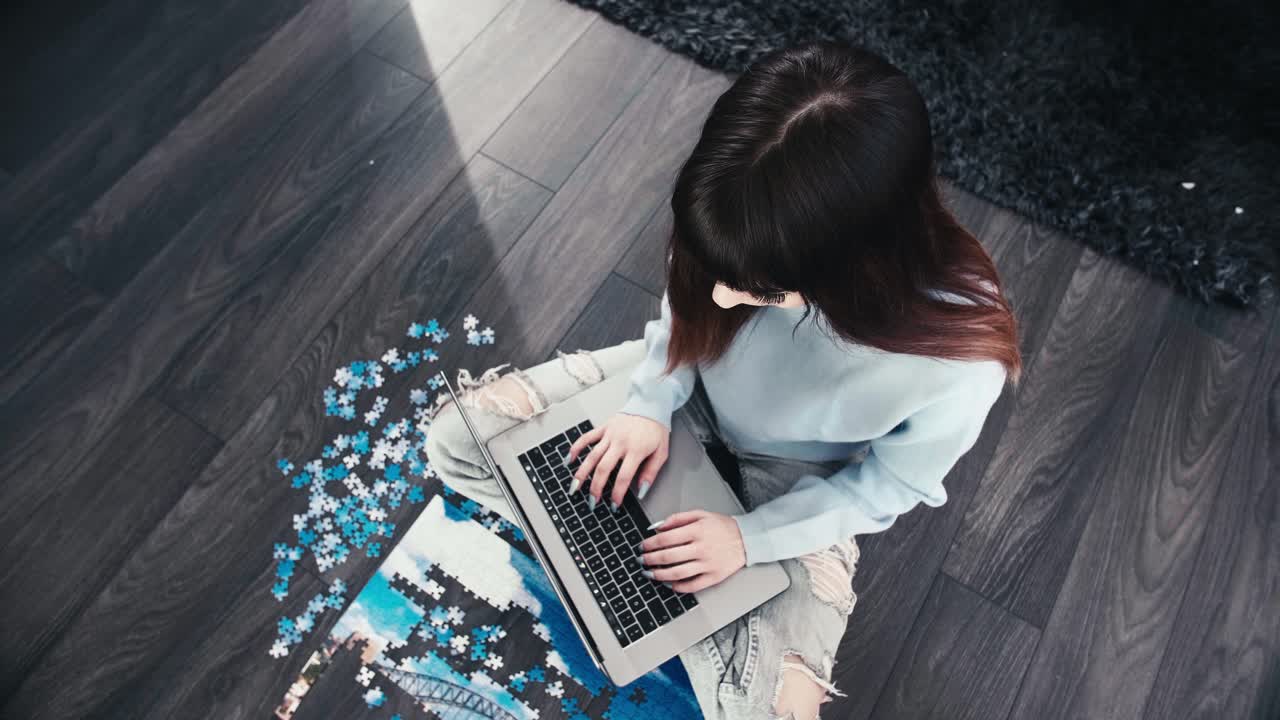 Young modern woman typing fast on her modern laptop sitting cross legged in wooden parquet room