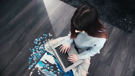 Young-modern-woman-typing-fast-on-her-modern-laptop-sitting-cross-legged-in-wooden-parquet-room