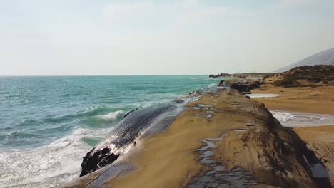 fast-moving-aerial-shot-alongside-the-coast-beach-erosion-in-mud-dry-mountain-rock-sea-wave-splash-in-summer-ocean-climate-in-tropical-island-Hormuz-in-Iran-Qatar-border-tourist-attraction-resort-hike