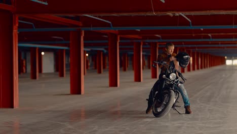 biker puts a helmet on his head, sits on a motorcycle in a large garage. circular motion of the camera.