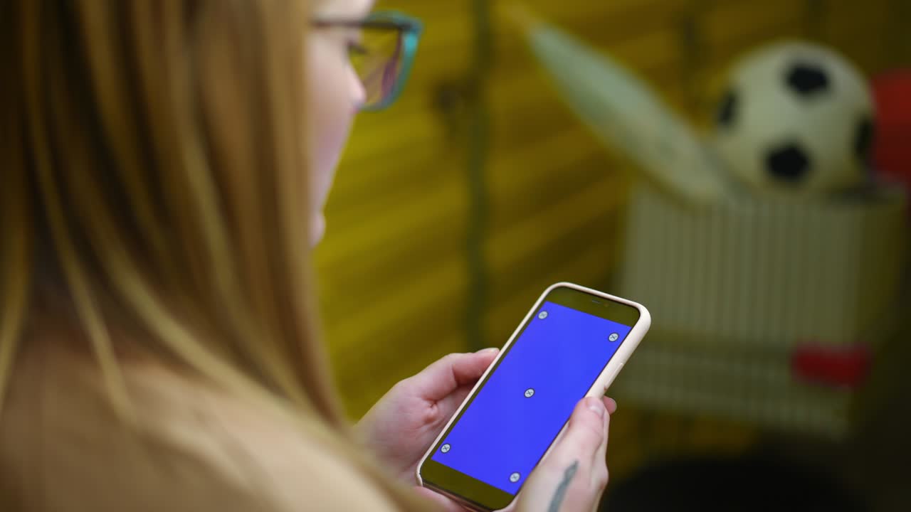 teléfono inteligente con pantalla azul en manos jóvenes femeninas tatuadas en el interior. mujer caucásica borrosa navegando por internet en línea usando aplicación en el teléfono de pie en el almacén amarillo de almacenamiento automático.