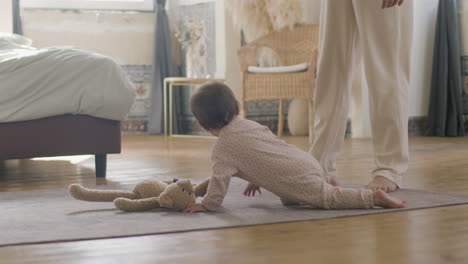 adorable little baby in pajamas crawling on bedroom floor while her mother looking after her