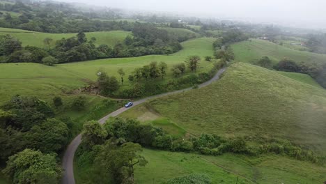 driving-through-mountains-in-modern-SUV-car,-aerial-video,-drone,-driving-in-foggy,-green-mountains