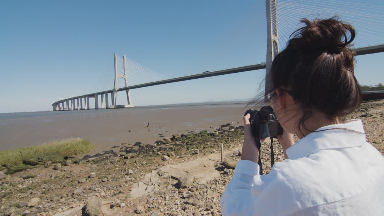 Young woman taking a photo of the Tagus river and Vasco da Gama bridge in Lisbon, Portugal