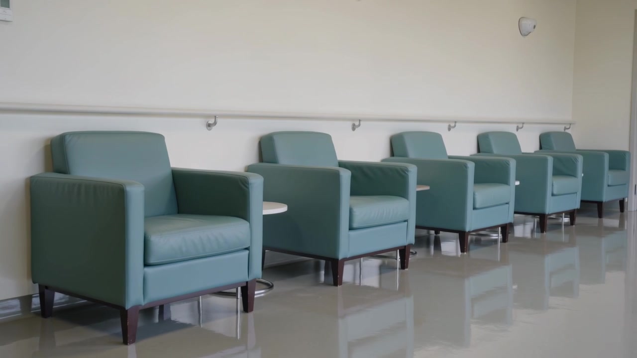 Panning camera revealing row of teal armchairs in care corridor to reveal seating with side tables