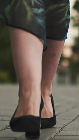Graceful young woman in stylish black shoes and skirt waved by strong wind walks along paved road on spring day extreme close view