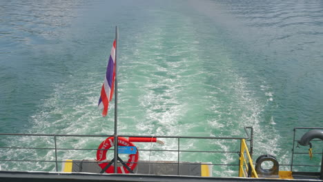 thai flag waves in wind as ship departs from dock with small wake trailing