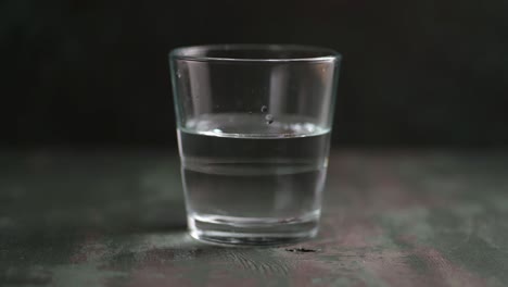 vertiendo agua en un vaso transparente sobre el fondo oscuro