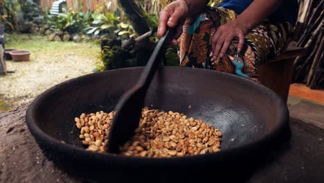 medium shot of beans of the expensive kopi luwak coffee being stirred and roasted in a wok with a wooden spoon by an employee of a coffee plantation in ubud, bali in indonesia