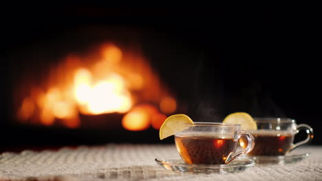 Two-Cups-Of-Tea-With-Lemon-On-The-Background-Of-The-Fireplace-Stand-On-A-White-Knitted-Tablecloth