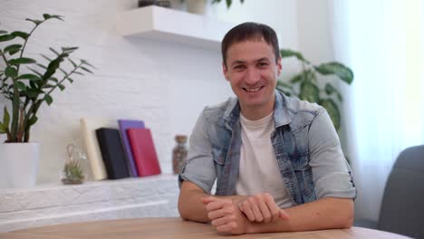 Head-shot-millennial-guy-sit-in-living-room-makes-video-call-looks-at-camera,-conversation-by-distant-videocall,-distance-hiring-job-interview-process,-tutor-and-trainee-study-on-line