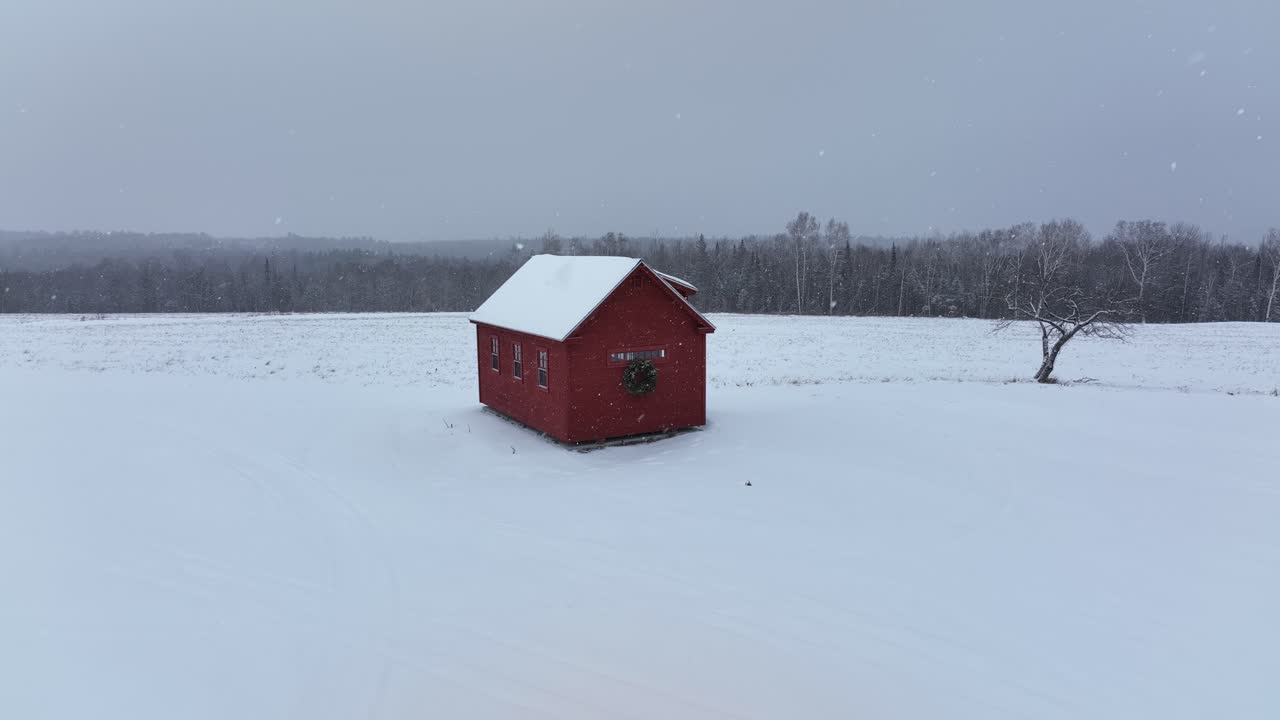 Little red cabin sits against a forest backdrop light dusting of snow