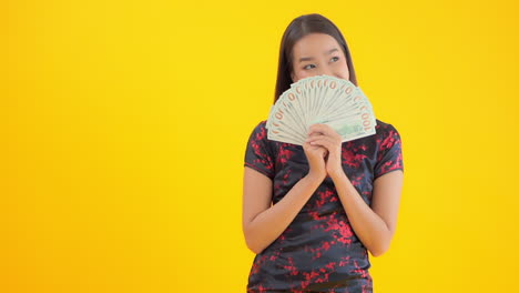 a beautiful asian woman in a black and red silk dress hides her face behind a fan of hundred dollar bills