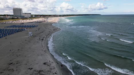 Hermosa-Playa-En-El-Mar-Báltico,-La-Gente-Camina-Por-La-Playa,-Las-Olas-Golpean-La-Costa,-Warnemünde,-Drone