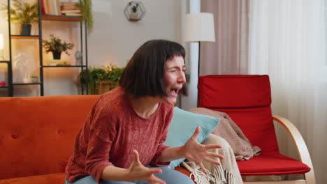sad woman feeling hopelessness loneliness nervous breakdown crying shouting while sitting on sofa