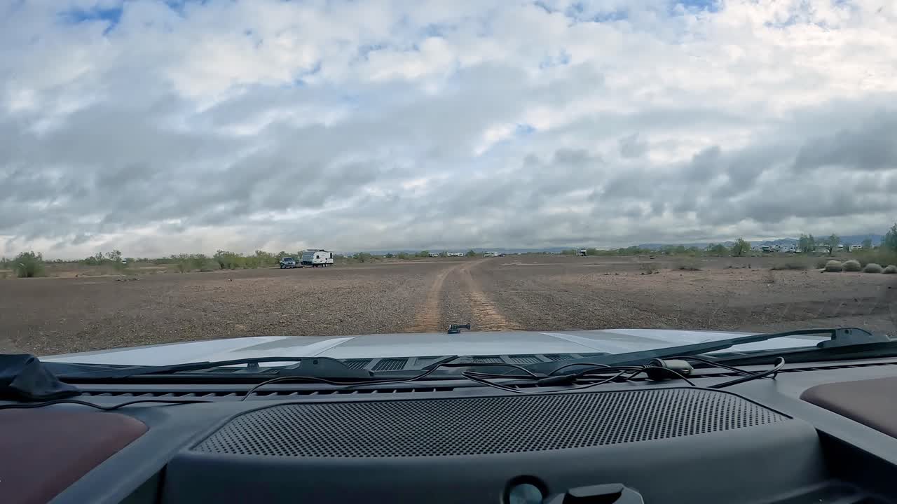 pov conduciendo en un sendero de grava a través del desierto de sonora en el suroeste de arizona hacia grupos de campistas dispersos en un día nublado de invierno