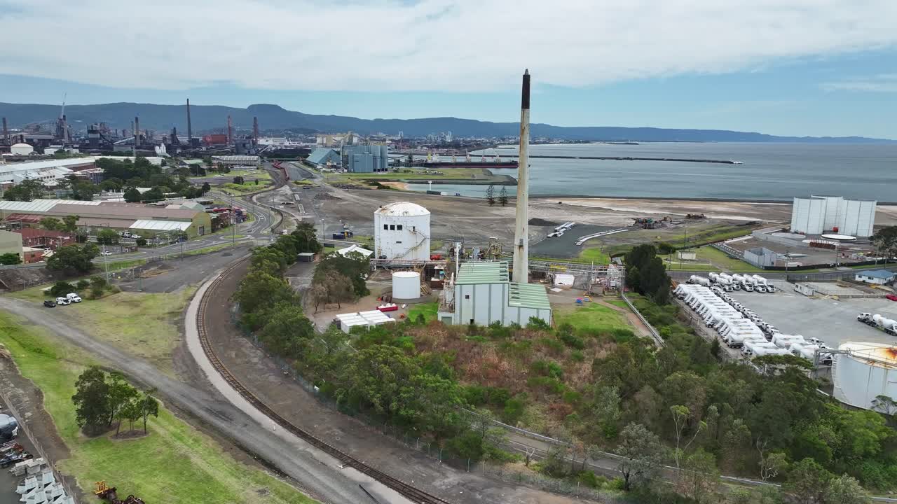 Aerial of Port Kembla industrial area with large chimney storage tanks and wharves beyond