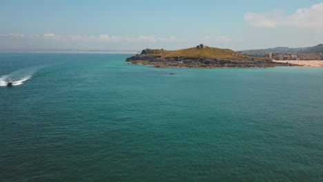 Speedboat-in-turquoise-sea-waters-off-Cornwall-rugged-coast,-summer-aerial-view