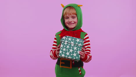 cheerful girl in santa sweater presenting one christmas gift box, stretches out her hands to camera