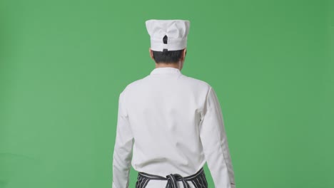 vista trasera del chef asiático caminando en el estudio de fondo de la pantalla verde