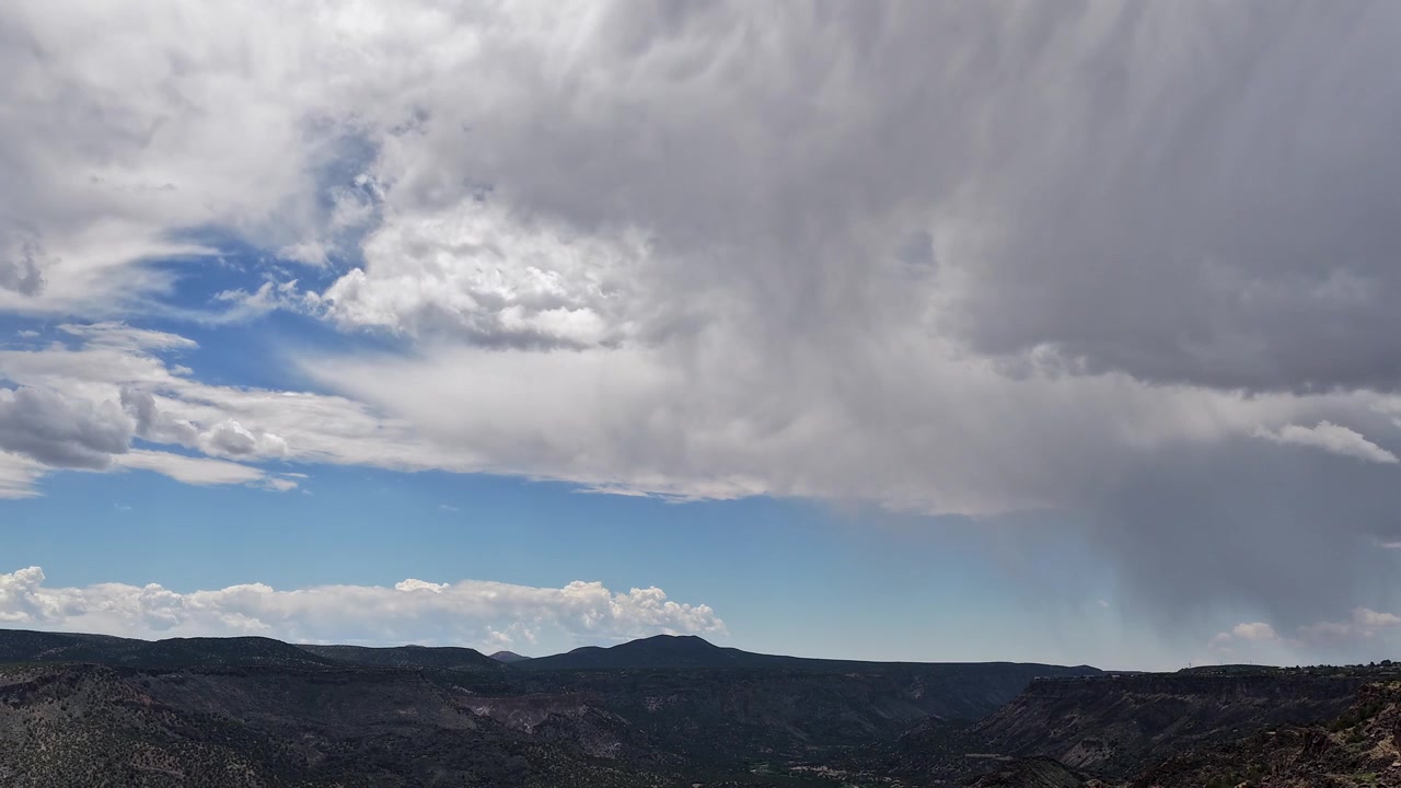 Timelapse 4K panoramico con drone di un drammatico temporale che si avvicina a un aspro canyon nel sud-ovest. Nuvole temporalesche atmosferiche si addensano mentre scuri scrosci di pioggia si abbattono sulla maestosa gola profonda e sull'altopiano desertico.