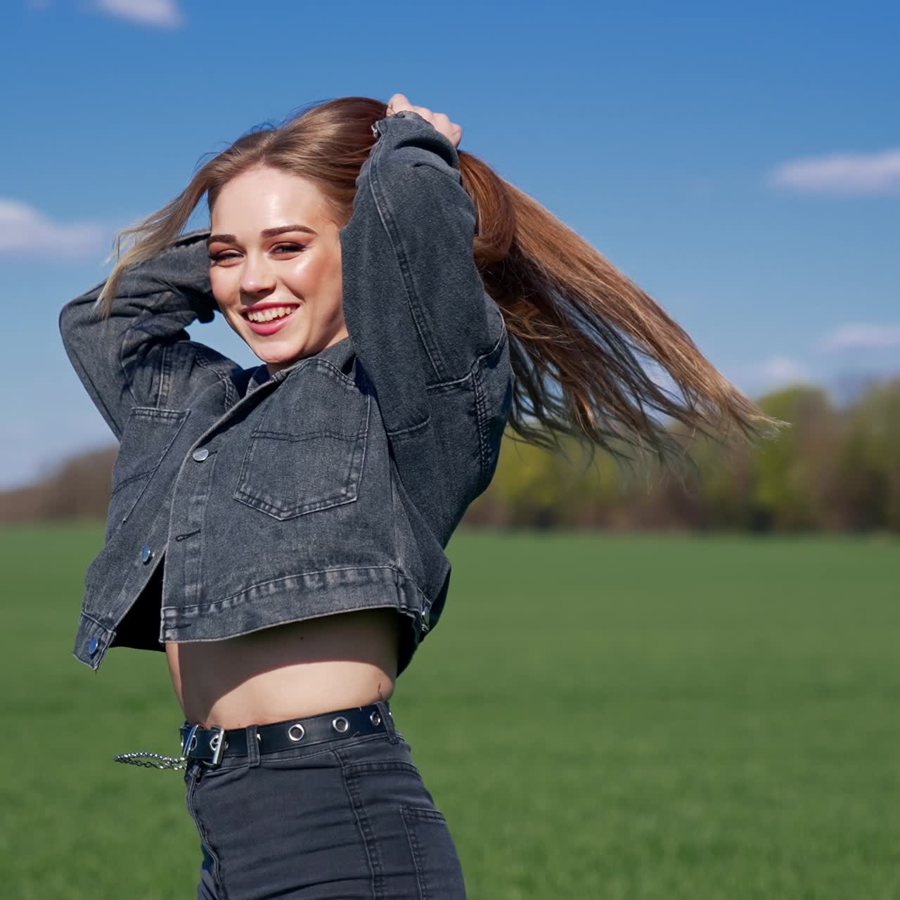 Happy girl on a meadow. Attractive young model with lovely face in denim suit posing on camera and smiles. Portrait of a young woman in nature in a sunny day