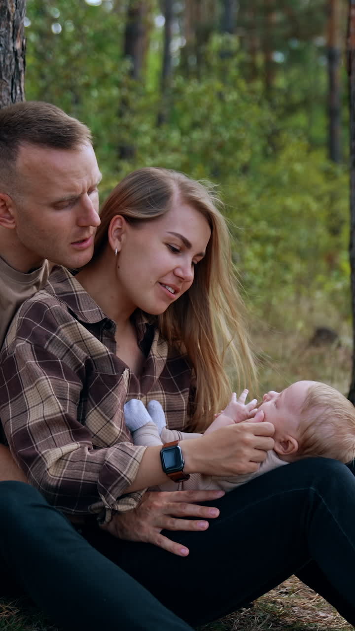 Caring parents calming down their crying baby. Mom and dad nursing their child spending time in nature. Vertical video